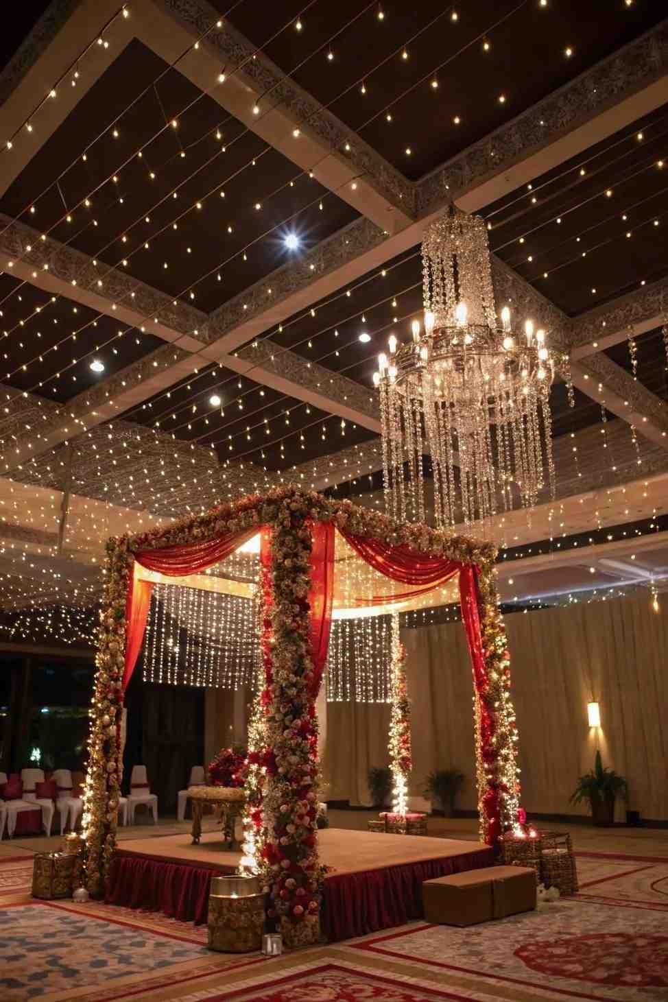 Indoor wedding mandap with crystal chandelier and fairy lights.
