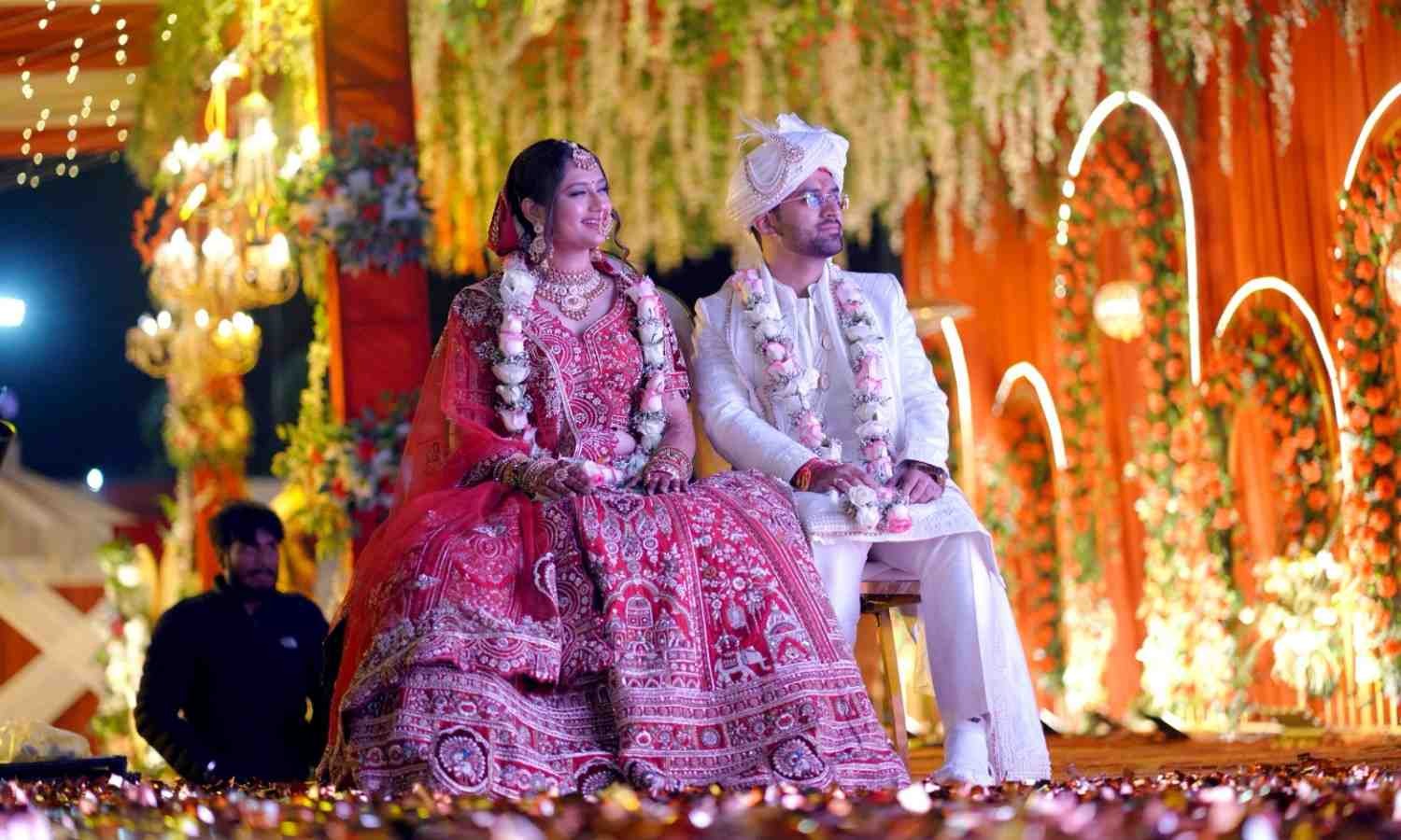 Bride and groom sitting on a beautifully decorated wedding stage with floral d&eacute;cor and lights during an Indian wedding ceremony.