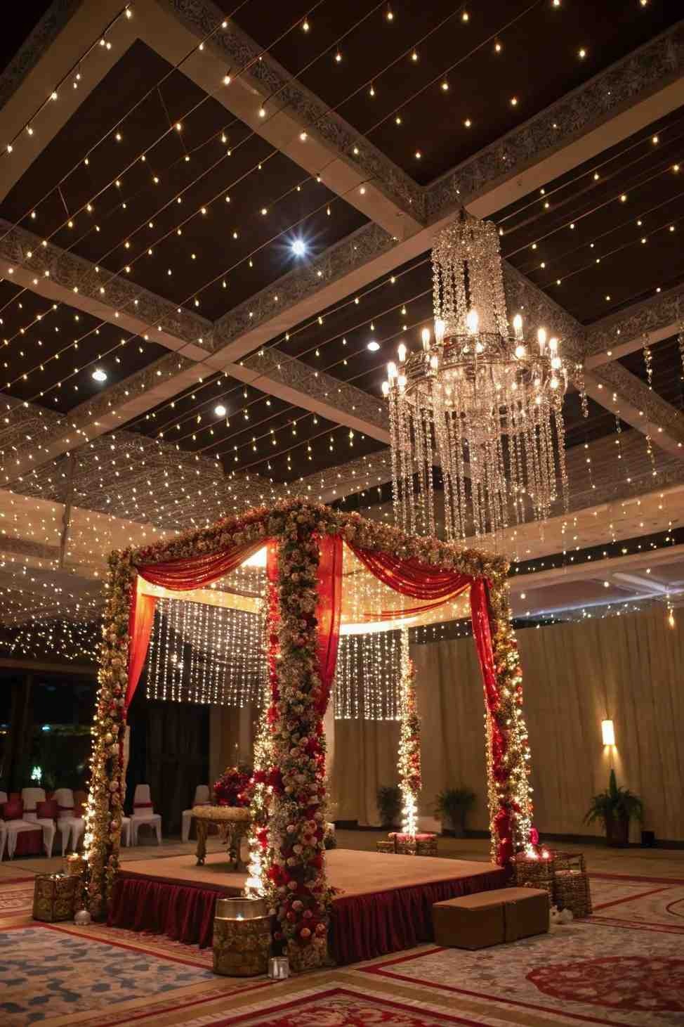 Luxury floral wedding mandap with crystal chandelier, fairy lights, and elegant indoor wedding decor.