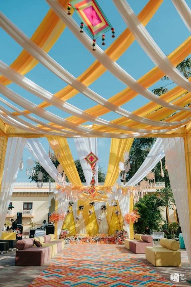 Bright yellow and white haldi ceremony decor with draped canopy, floral backdrop, and elegant outdoor wedding seating.
