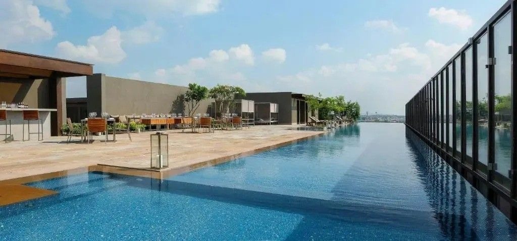 Stunning rooftop infinity pool at Roseate House Aerocity, New Delhi India: sleek blue lap pool with city skyline views, modern tan loungers, wooden dining sets, stylish bar counter.
