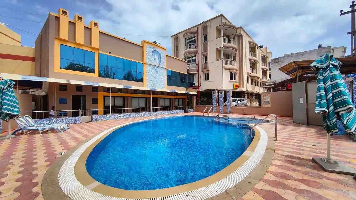 Hotel Samrat International Chanakyapuri New Delhi swimming pool: oval-shaped turquoise pool with dolphin mosaic wall art, yellow building facade with blue glass windows.