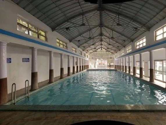 Delhi Gymkhana Club Swimming Pool in New Delhi India: elegant indoor lap pool with clear turquoise water, classic white columns with brown bases along blue-trimmed walls.