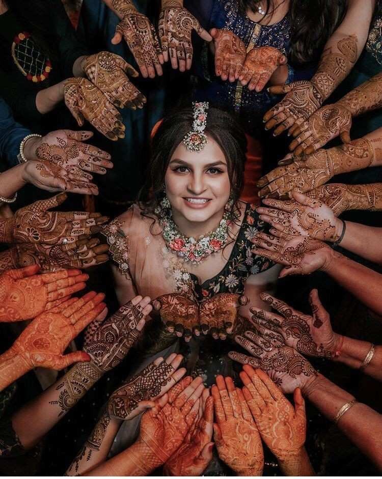 Bride surrounded by friends displaying beautiful bridal mehndi designs during wedding mehendi ceremony with intricate henna art and festive celebration vibes.