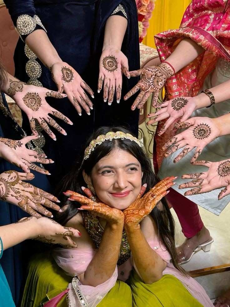 Bride surrounded by friends showing stylish mehndi designs during wedding mehendi ceremony celebration with traditional henna art and festive outfits.