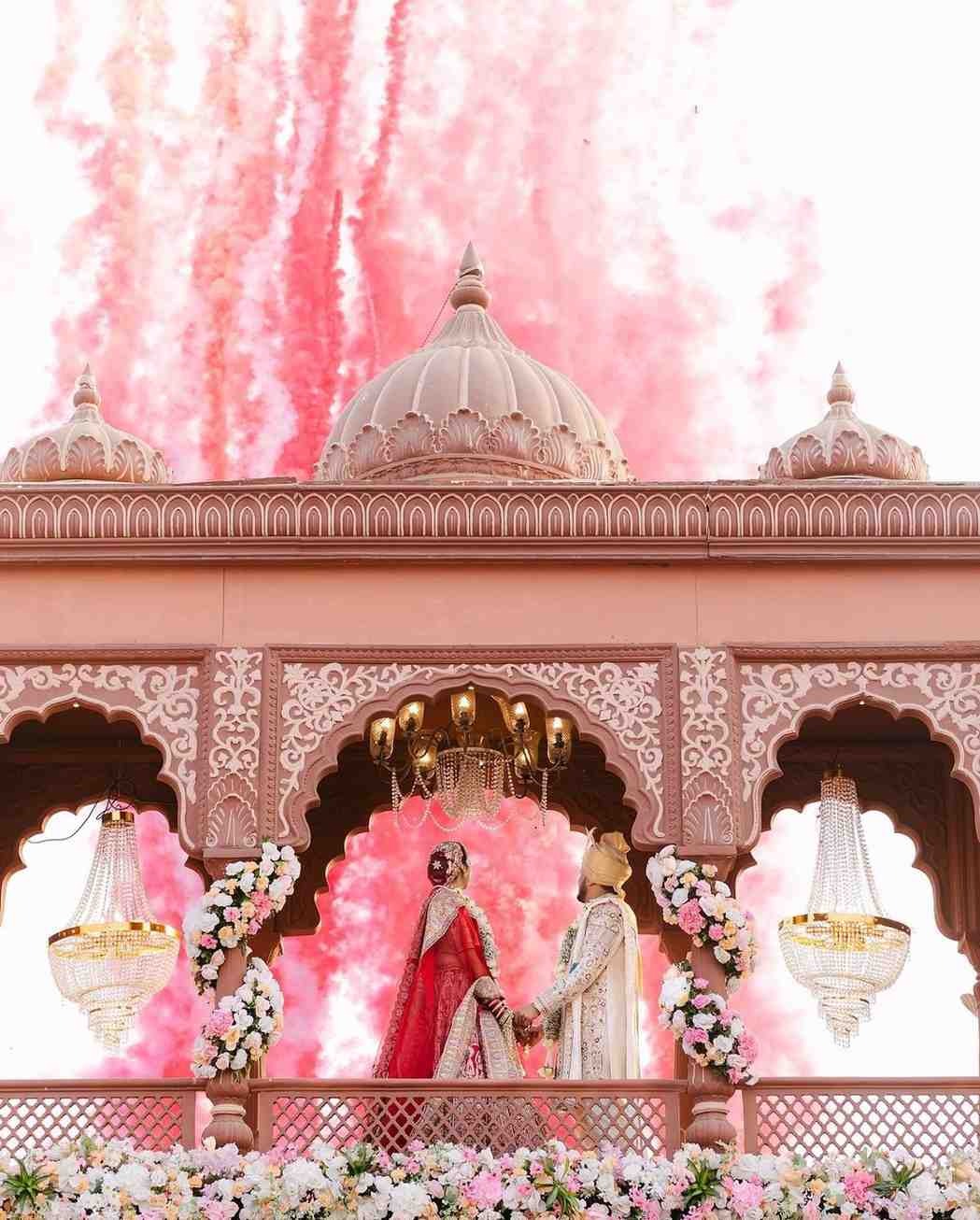 Royal couple wedding portrait with pink fireworks backdrop at luxury palace venue.