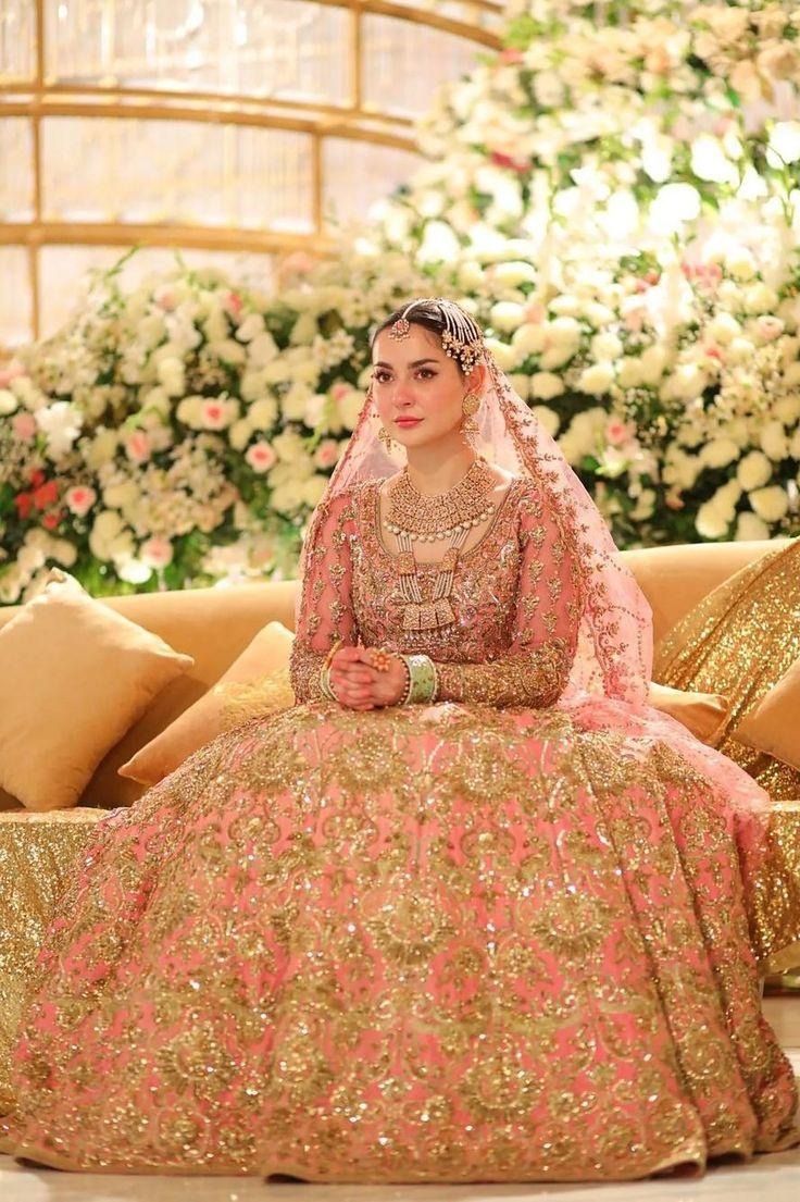 Bridal lehenga in blush pink featuring heavy zari embroidery, statement jewelry, and elegant floral wedding décor.