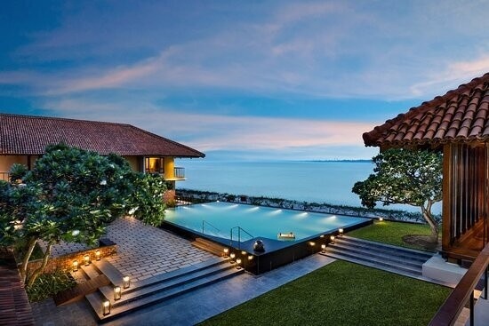 "Luxury waterfront villa with infinity pool, ocean view, modern architecture, ambient lighting, and peaceful sunset scenery."