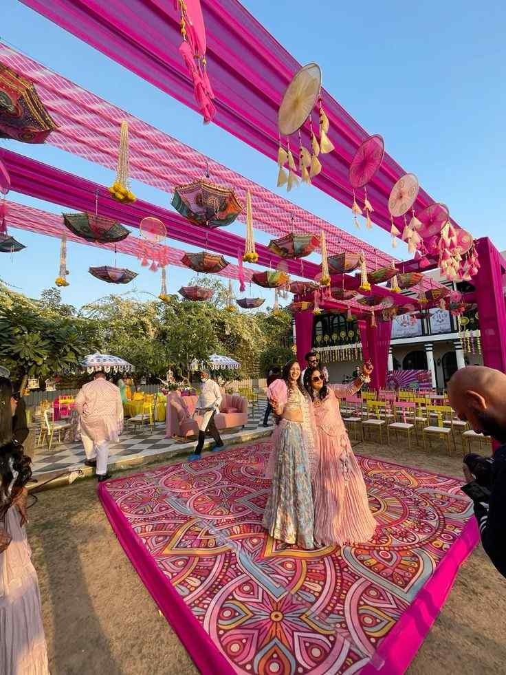 Colorful outdoor Mehndi ceremony setup with vibrant pink drapes, hanging umbrellas, decorative dance floor, and premium wedding decor at a luxury venue in Delhi NCR.