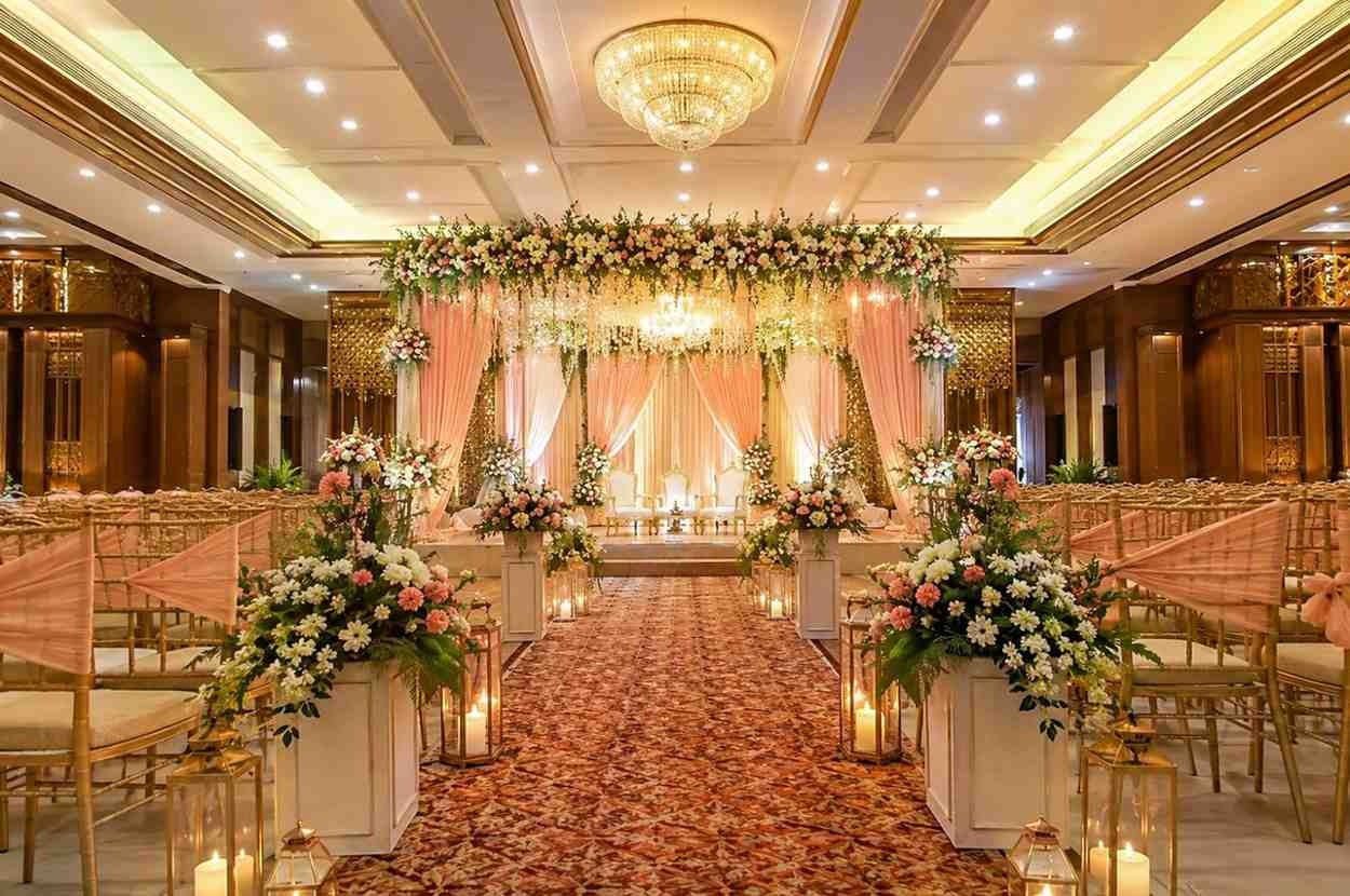 Luxury wedding banquet hall with a beautifully decorated floral stage, grand chandelier, flower-lined aisle, elegant seating arrangement, and premium indoor wedding décor.