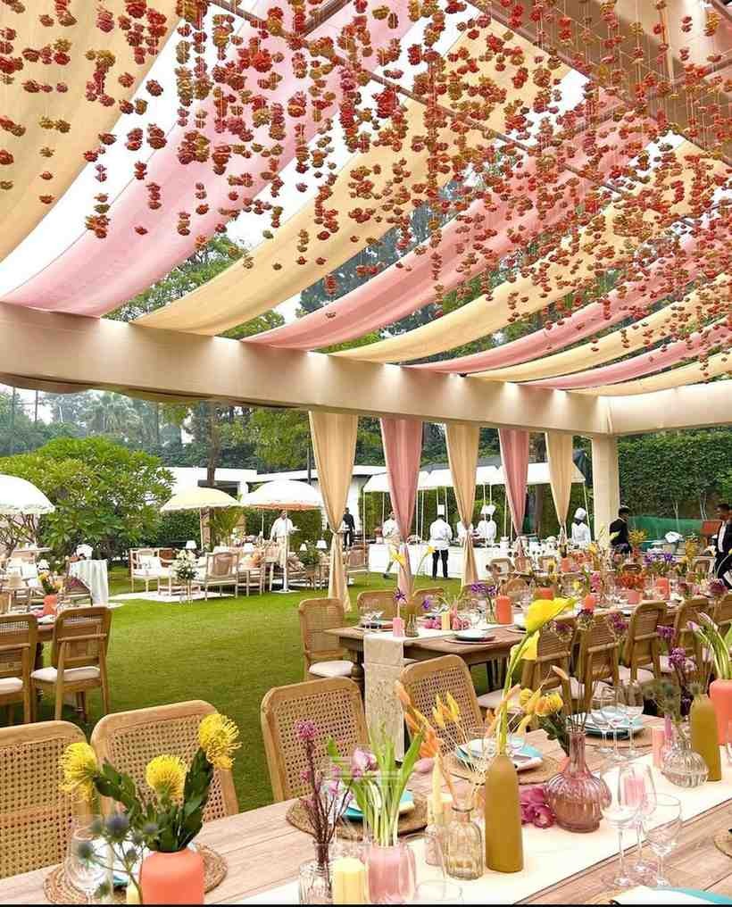 Beautiful outdoor garden wedding venue with floral hanging decor, elegant dining setup, lush green lawn, and luxury seating arrangement for weddings, receptions, and engagement celebrations in Delhi NCR.
