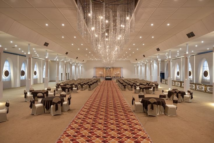 Spacious luxury banquet hall with elegant chandelier, stage setup, and seating arrangement for weddings, receptions, and corporate events.